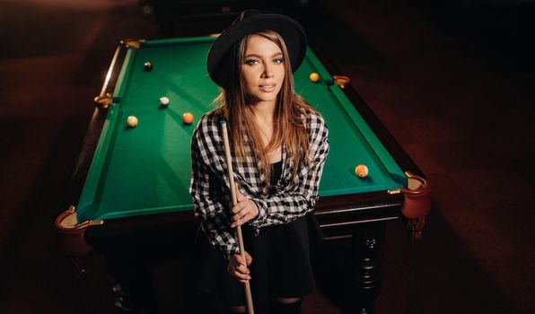 A girl in a hat in a billiard club with a cue in her hands.billiards Game.