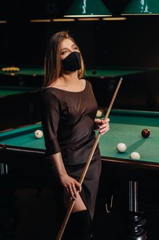 Masked girl in a pool club with a cue in her hands.