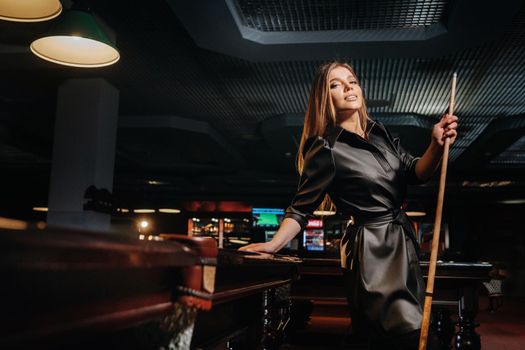 A girl with a cue in her hands is standing in a billiard club.Russian billiards.