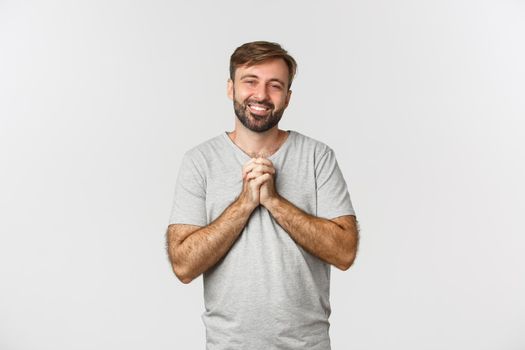 Image of handsome thankful man, holding hands together and expressing gratitude, smiling pleased, standing over white background.