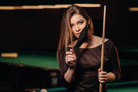 Masked girl in a pool club with a cue in her hands.