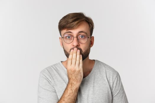 Close-up of surprised man in glasses, gasping and looking at camera concerned, standing over white background.