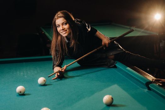 A girl with a cue in her hands makes a shot at a ball in a billiard club.Russian billiards.