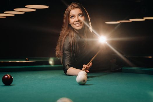 A girl with a cue in her hands makes a shot at a ball in a billiard club.Russian billiards.