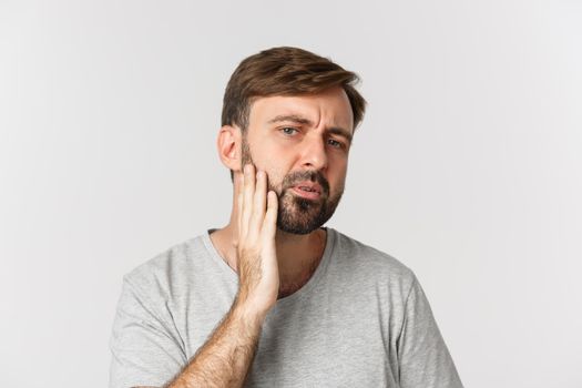 Close-up of confused man touching his beard and looking at himself, need to shave, standing over white background.