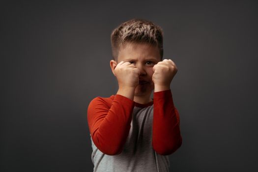 Sad preschool kid expresses anger. Little boy holds his fists in front of him to attack or defend. Conflict concept. Fight concept.