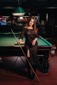 A girl in a hat in a billiard club with a cue in her hands.Pool Game.