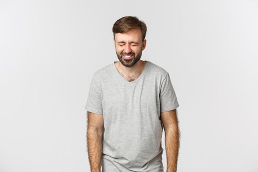 Image of cheerful bearded guy in gray t-shirt, laughing and having fun, standing over white background.