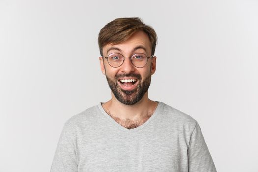 Close-up of handsome modern guy in glasses, looking excited and amused, standing over white background.