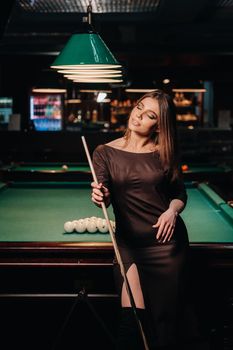 A girl in a hat in a billiard club with a cue in her hands.Pool Game.