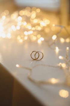 Wedding rings on blured bokeh glowing golden background. Symbol of love and romance on a textured glitter background with copy space for your greeting or congratulations.