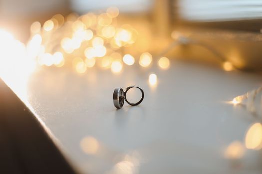 Wedding rings on blured bokeh glowing golden background. Symbol of love and romance on a textured glitter background with copy space for your greeting or congratulations.