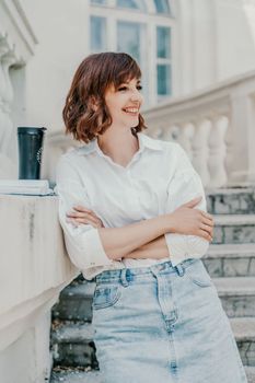 Woman building city. A business woman in a white shirt and denim skirt stands leaning against the wall on the steps of an ancient building in the city.