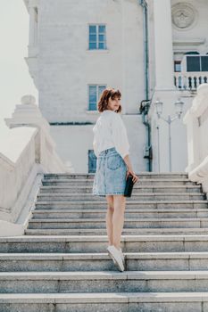 Woman staircase city. A business woman in a white shirt and denim skirt walks down the steps of an ancient building in the city.