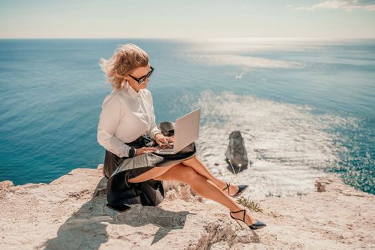 Business woman on nature in white shirt and black skirt. She works with an iPad in the open air with a beautiful view of the sea. The concept of remote work