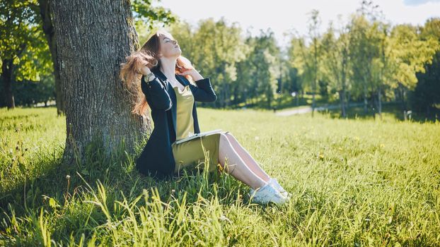 A girl with a laptop resting in the park by a tree