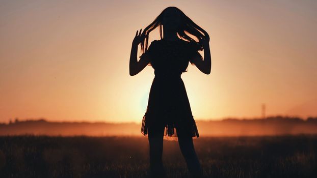 A silhouette of a young girl dancing and spinning on a warm summer evening at sunset