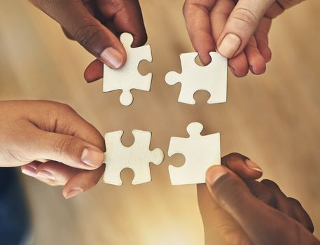 Piece by piece. High angle shot of four unrecognizable businesspeople building a jigsaw puzzle