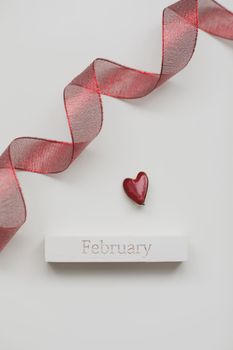 Greeting card with word February. Red ribbon and heart on white wooden background, flat lay.