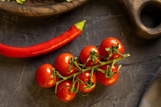 Delicious ripe cherry tomatoes, chili peppers and garlic for cooking on a dark background. Top view.