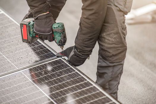 The solar panel installer twists the modules together using aluminum fasteners and a cordless drill. Rooftop installation work and security, concept with copy space.