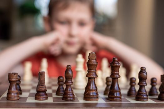 Young white child playing a game of chess on large chess board. Chess board on table in front of school boy thinking of next move, tournament