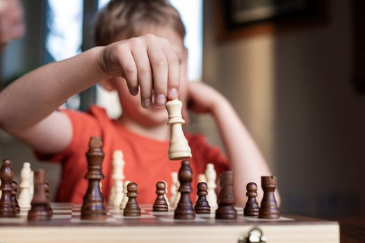 Young white child playing a game of chess on large chess board. Chess board on table in front of school boy thinking of next move, tournament