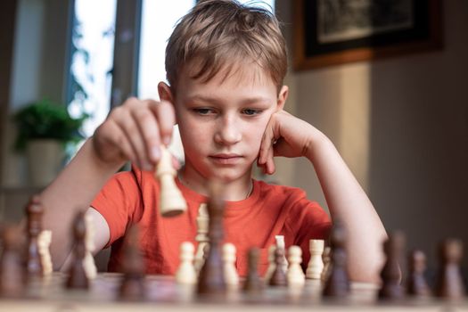 Young white child playing a game of chess on large chess board. Chess board on table in front of school boy thinking of next move, tournament