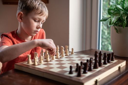 Young white child playing a game of chess on large chess board. Chess board on table in front of school boy thinking of next move, tournament