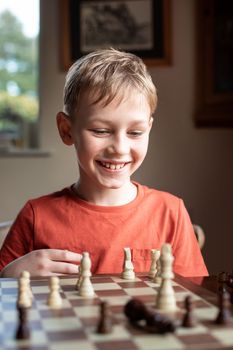 Young white child playing a game of chess on large chess board. Chess board on table in front of school boy thinking of next move, tournament