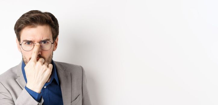 Serious boss in suit frowning, put on glasses and looking suspicious at camera, white background.