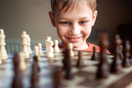 Young white child playing a game of chess on large chess board. Chess board on table in front of school boy thinking of next move, tournament