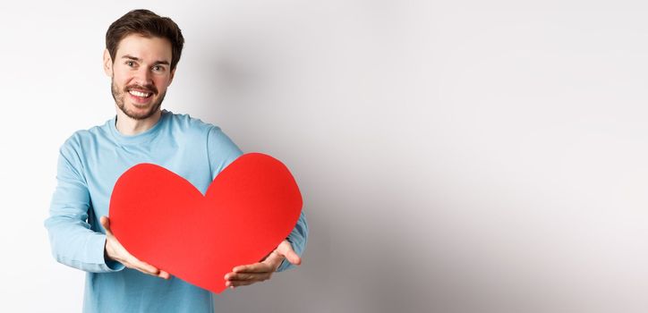 Happy gay man giving big red heart to his lover on valentines day, concept of romantic date and love celebration, standing over white background.