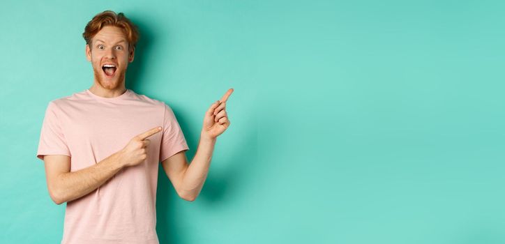 Excited guy in pink t-shirt showing advertisement on mint background, looking amazed at camera and pointing at upper right corner.