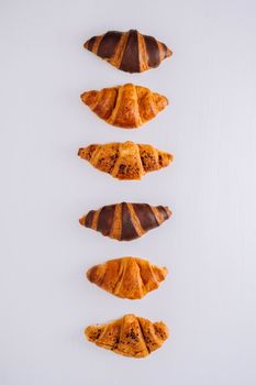 Flat lay of several delicious brown and chocolate croissants laid out in a line on white table