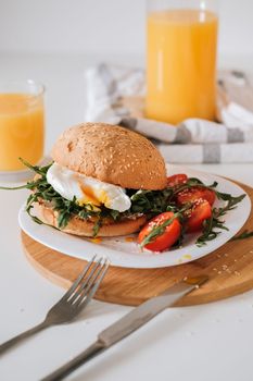 Breakfast sandwich with egg and arugula and cherry tomatoes on table with orange juice