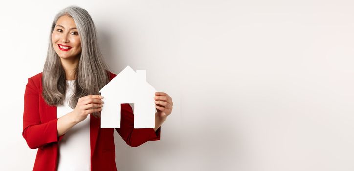 Smiling real estate agent showing paper house clipboard, broker working with client, standing over white background.