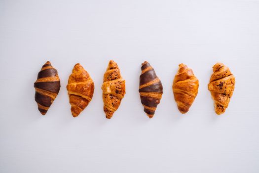 Flat lay of several delicious brown and chocolate croissants laid out in a line on white table