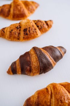 Close up of bunch of delicious brown and chocolate croissants laid out on white table