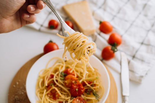 Spaghetti wrapped on fork in the background of a portion of pasta with cherry tomatoes in a plate and parmesan cheese
