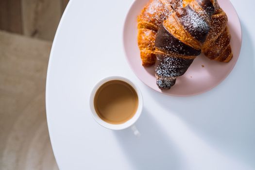 Flat lay cup of cappuccino and croissants on white coffee table in room with beautiful sunlight