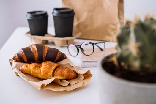 Delicious brown and chocolate croissants with coffee cup, having lunch at workplace, food delivery concept