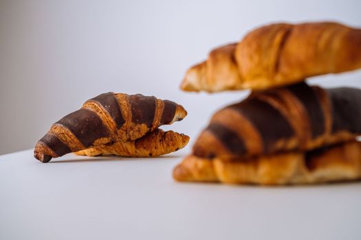 Bunch of delicious brown and chocolate croissants stacked on top of each other on white table