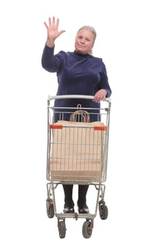 Full length shot of a senior lady waving and pushing an empty shopping cart isolated on white background