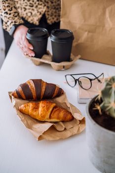 Delicious brown and chocolate croissants and coffee cup, woman having lunch at workplace, food delivery concept