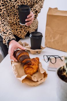 Woman at the workplace has lunch of brown and chocolate croissants with coffee, food delivery concept