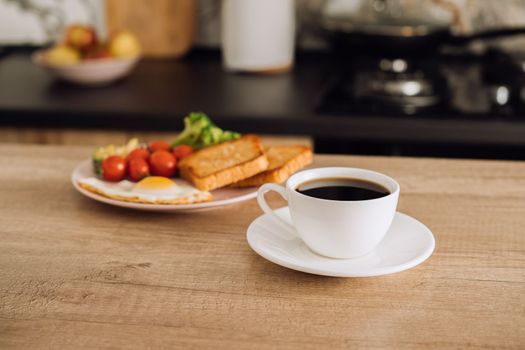 Cup of black coffee and breakfast in the background in kitchen at home