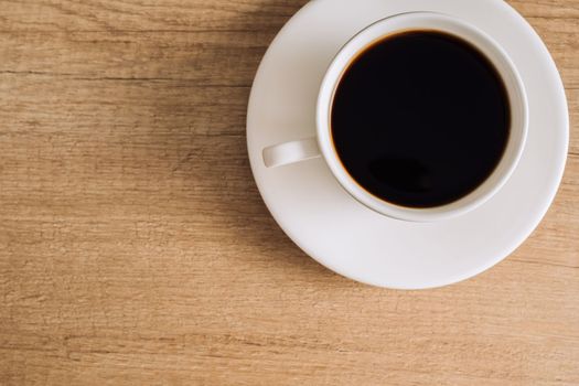 Black coffee in a white cup with a saucer on wooden table