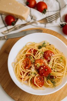Portion of spaghetti pasta with parmesan and cherry tomatoes sprinkled with spices in a plate on wooden board