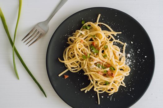 Spaghetti pasta sprinkled with cheese parmesan and green onions on a black plate on white table with fork